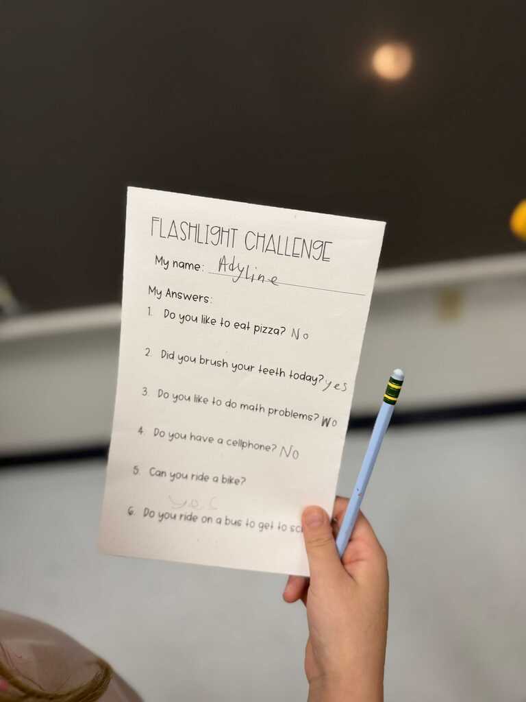 A hand holding a pencil and a sheet of paper with text about a flashlight challenge.