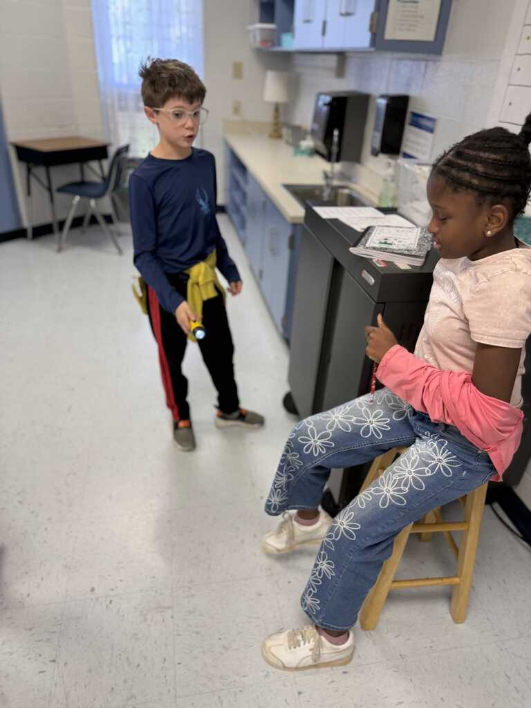 Two children, one standing and one sitting on a stool, appear to be discussing something.