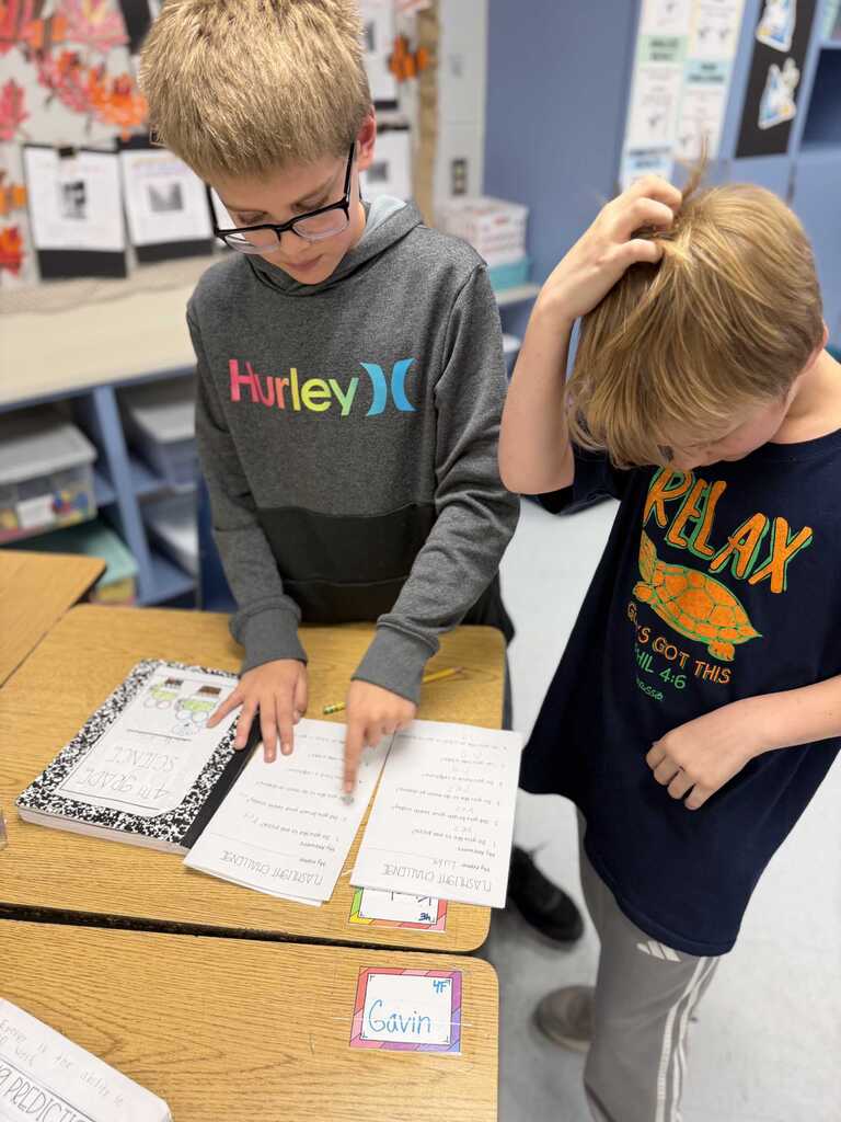 Two students at desks, one in glasses examining papers and another touching their hair.