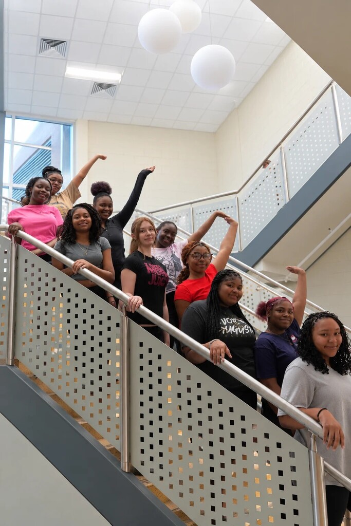 Girls standing on stairs with one hand up.
