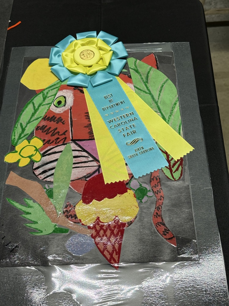 Artwork featuring colorful designs of leaves, ice cream, and a bird in plastic case. A blue ribbon with yellow center reads "1st Place" above the bird.