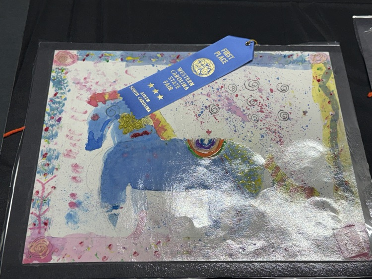Artwork on a glass table with a blue ribbon that reads "First Place". Painting shows an animal.