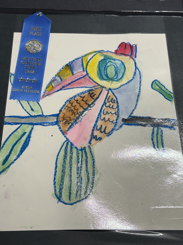 Drawing of a bird with colorful feathers on paper, displayed on a black background, with a blue ribbon.