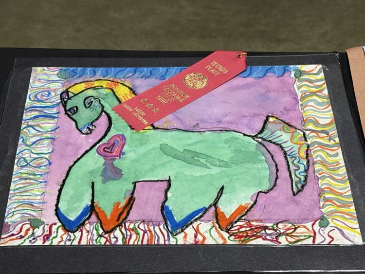 Display of a colorful painting of a unicorn with a red ribbon on top.