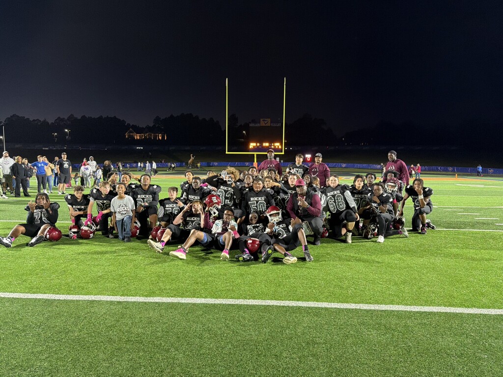 Football team posing for a group photo on a field, with the football goalposts in the background.