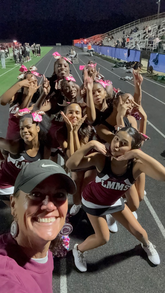 A group of cheerleaders with pink bows in hair posing for a photo on a track.