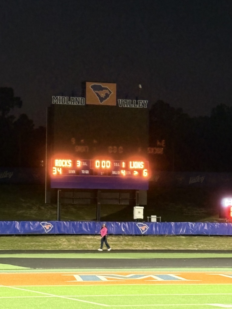 Nighttime scene with scoreboard displaying score. Person walking on field with illuminated path.