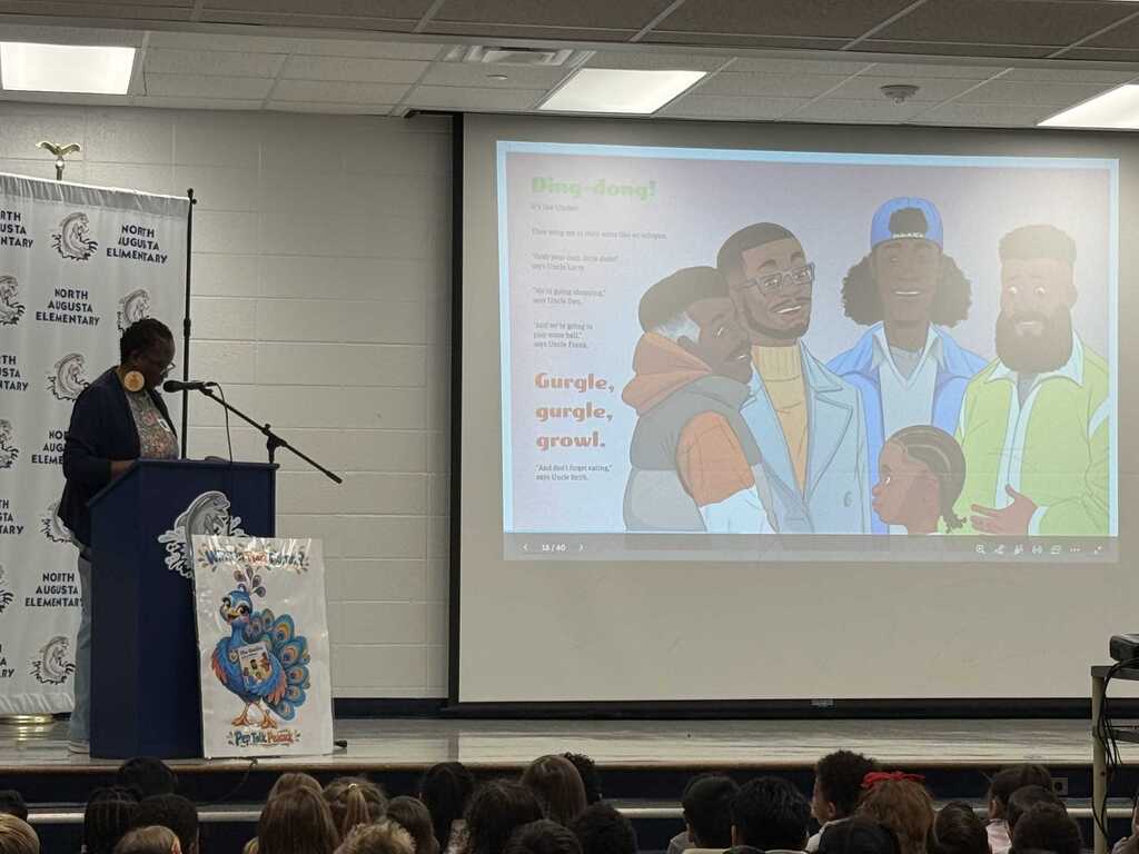 A person speaks at a podium with a microphone while a projector displays an image on a wall.
