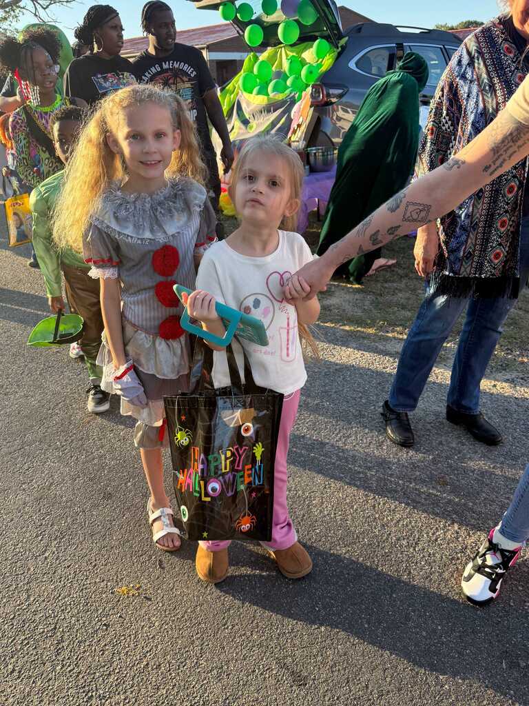 Two children walking in a parade, one holding a bag. People in the background.