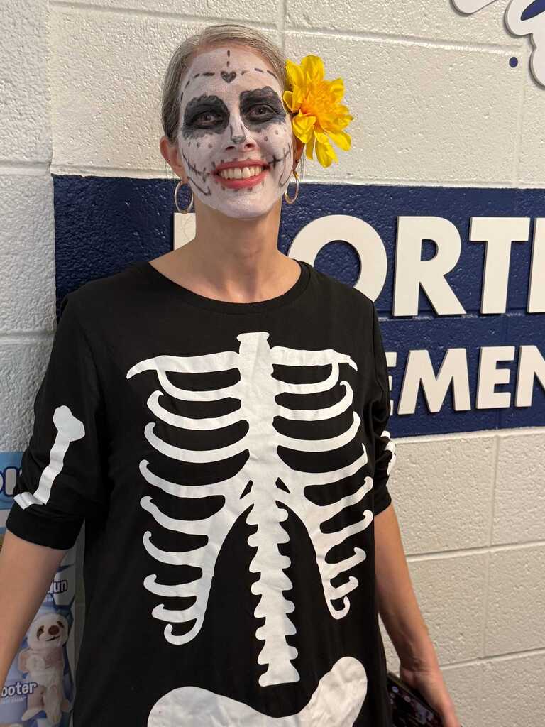 Person with face paint standing by wall, wearing a black shirt with a skeleton design.