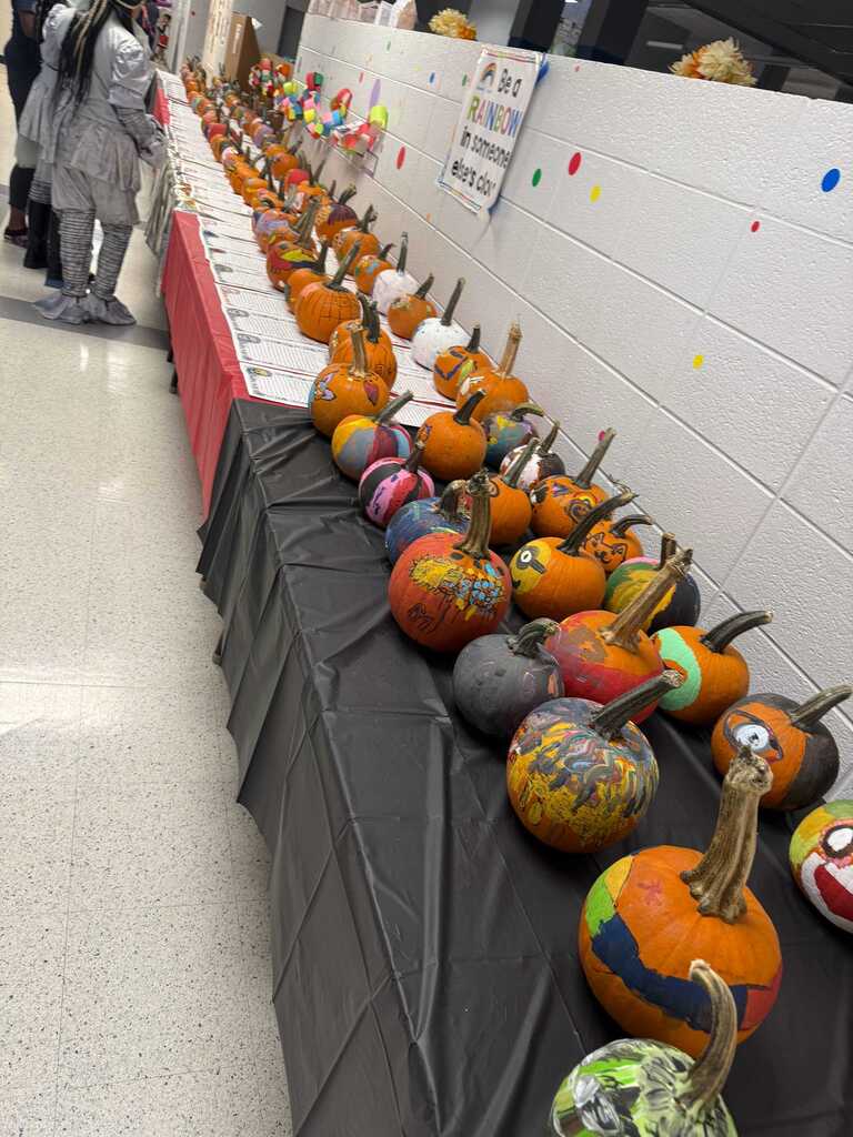 A hallway with a wall of colorful, painted pumpkins on black table cloths with a red cloth.