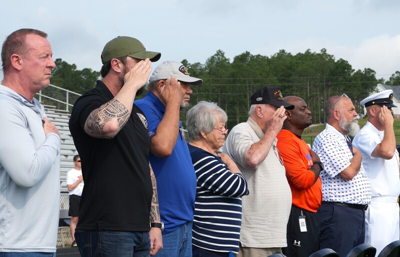 Community leaders, district leadership salute or place heart over their hand as they listen to the National Anthem.