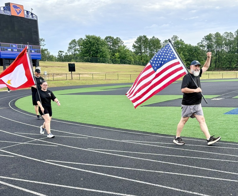 Principal Higgenbottom celebrating with a hand in the air while holding a US Flag.