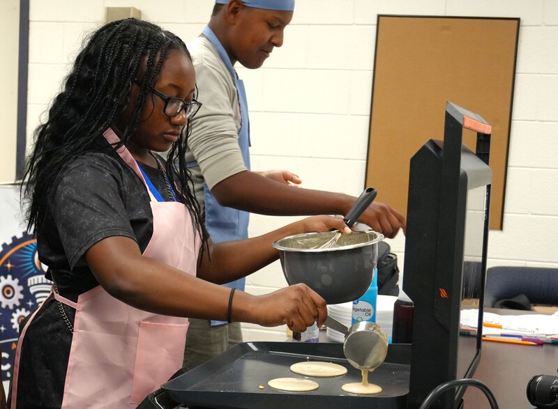Culinary students make pancakes on a griddle.