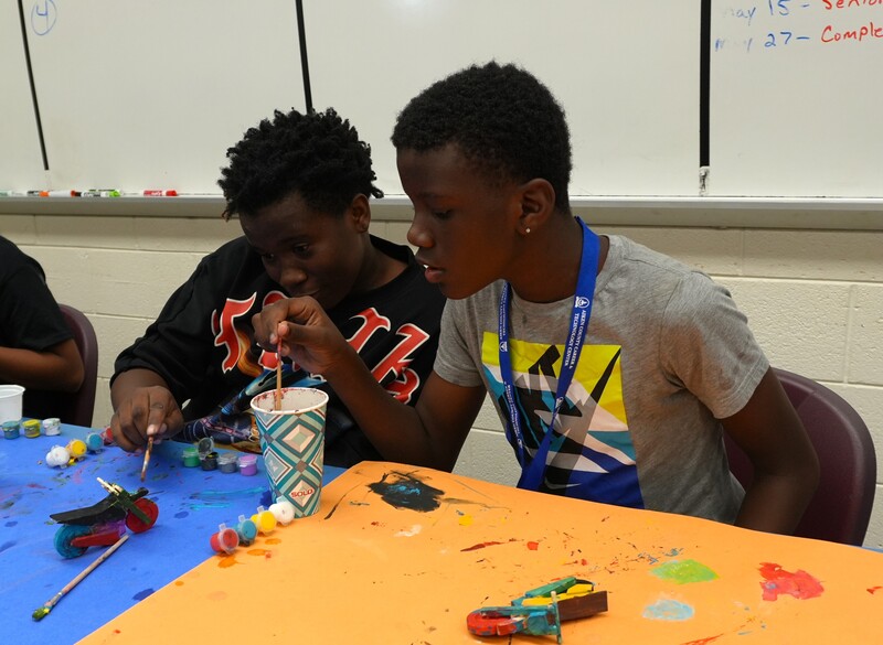 Two students work on painting a motorcycle.