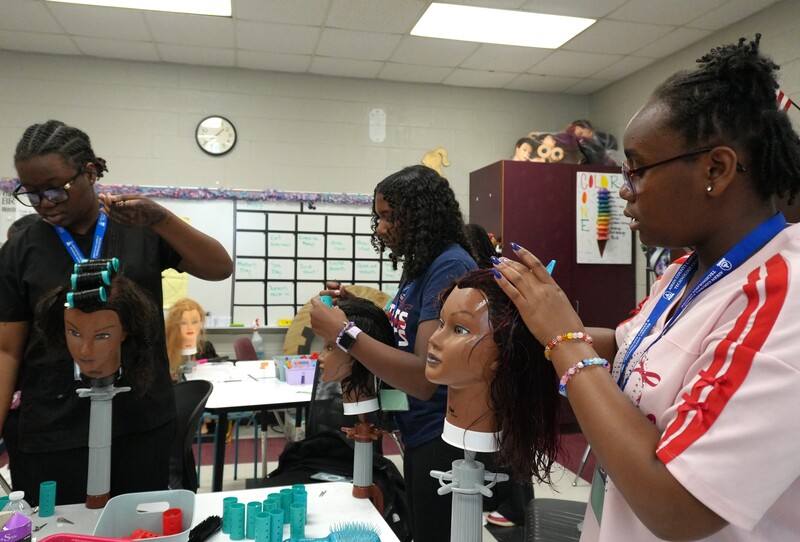 Students practice perming hair on mannequins.