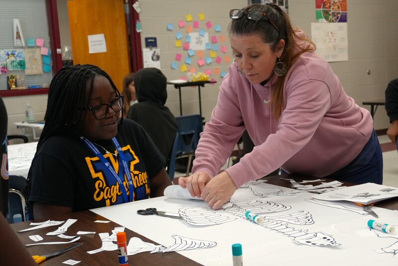 A teacher assists in labeling a skeleton.