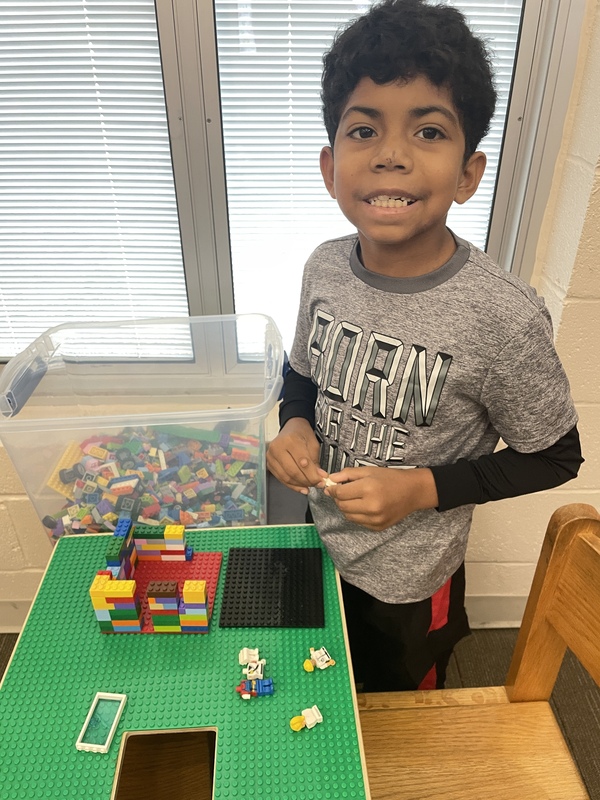 A smiling boy plays at a Lego table.