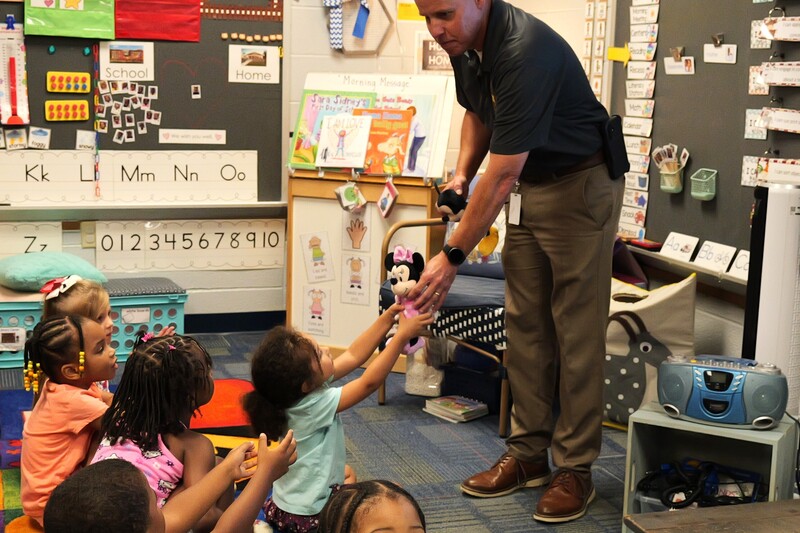 Officers handing a student a stuffed animal.