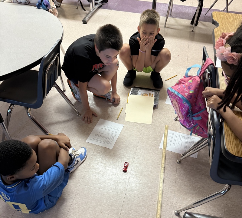 A group of students a watching a toy car after rolling down a ramp.