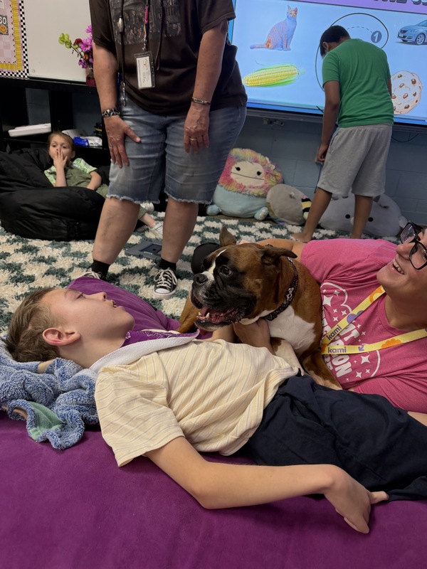 Ruby, the therapy dog snuggles with a boy on the floor.
