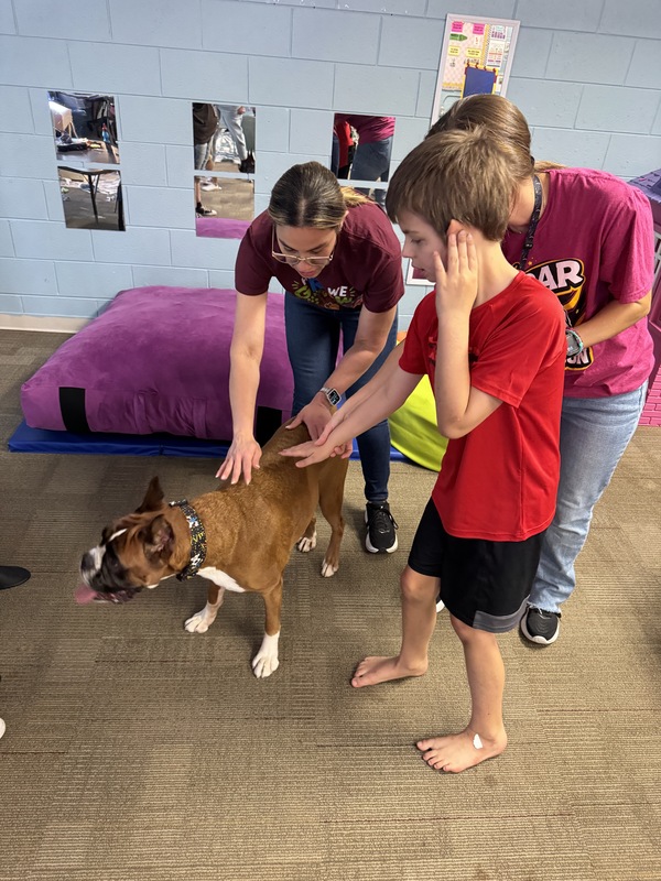 Two teachers stand with a student to pet Ruby, the therapy dog.