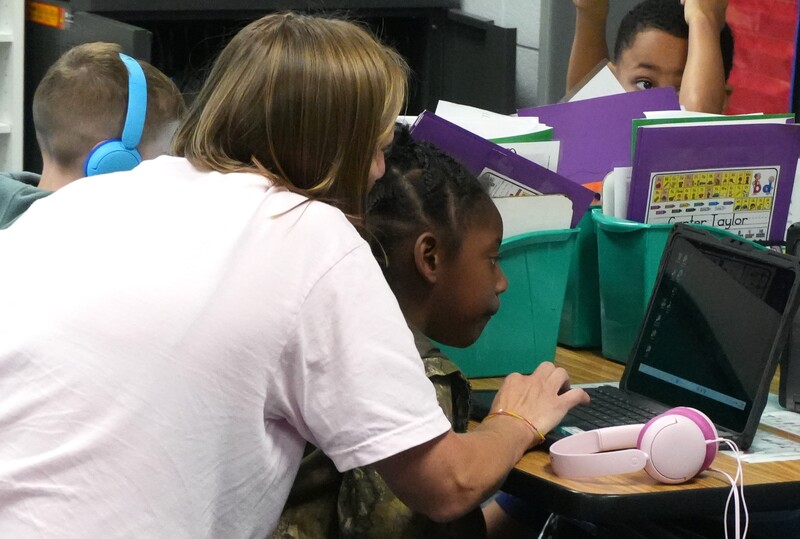 Aiken Elementary teacher Kari Keck assists a student using a laptop.