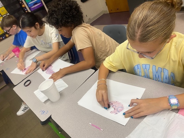Four students rub blackberries on their sheet of paper to reveal their hidden messages.