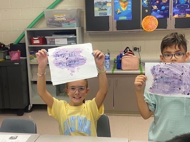 Two students hold up their sheets of paper to show their hidden messages.