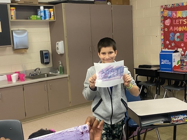A boy holds up his sheet of paper to show his hidden message.