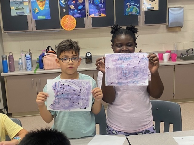 Two students hold up their sheets of paper to show their hidden messages.