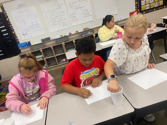 Four students use cotton swabs to write on a sheet of blank white paper.