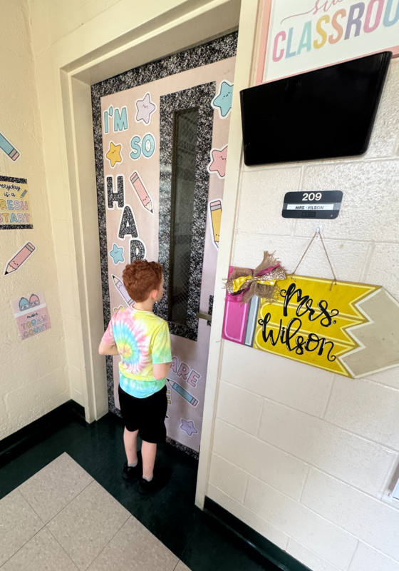 A boy stands outside a classroom door.