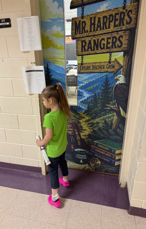 A girl holding a newspaper stands outside of a classroom door.