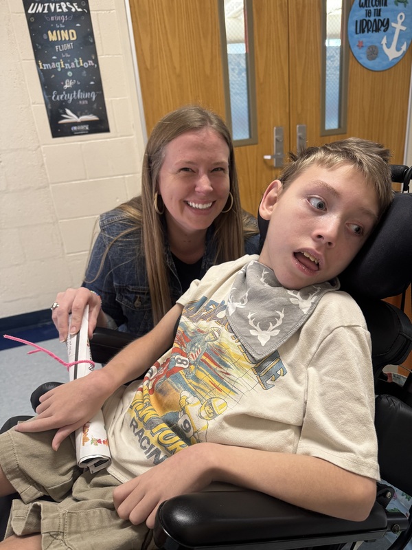 A teacher kneels next to a boy in a wheelchair.