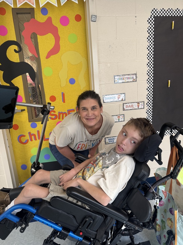 A teacher leans over a boy in a wheelchair.