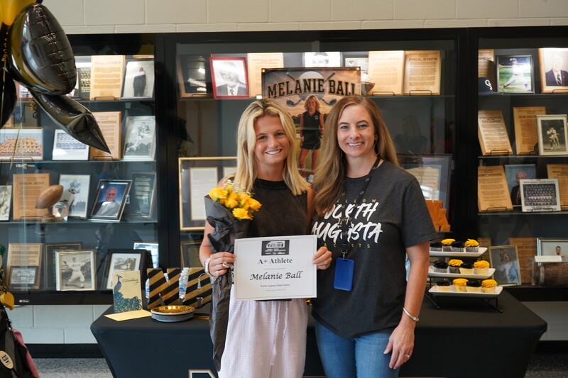 Student and Teacher in front of Award Case holding flowers and certificate.