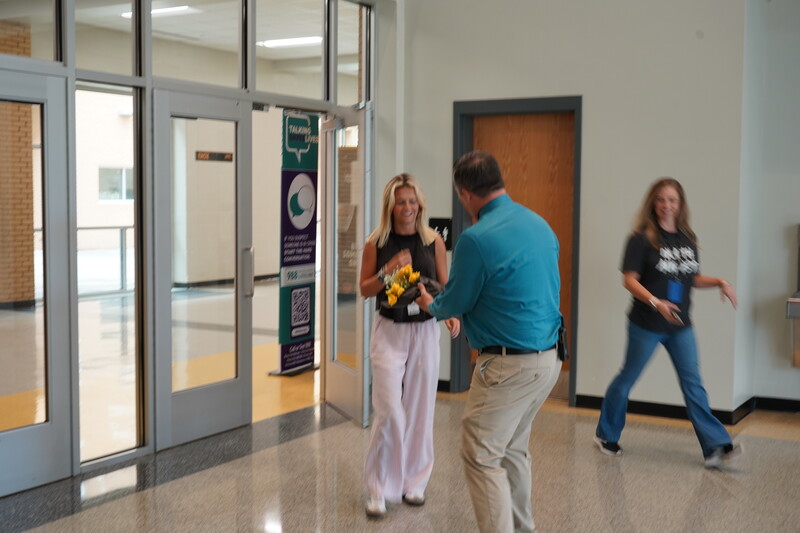 Principal handing flowers to female student with another staff member walking in background.