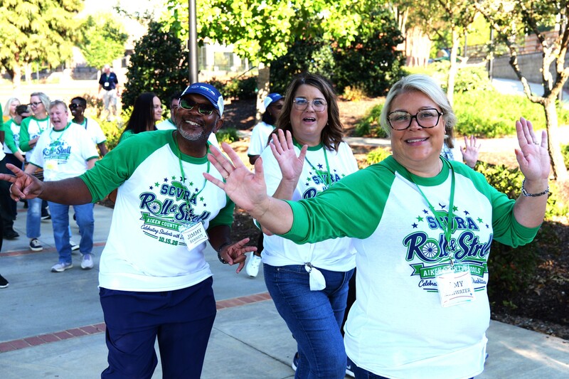 Three individuals wave to a camera.