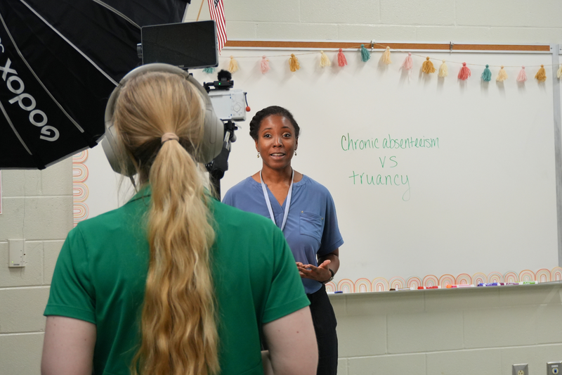 Teacher delivering lines in front of white board with chronic absenteeism vs truancy written on it.