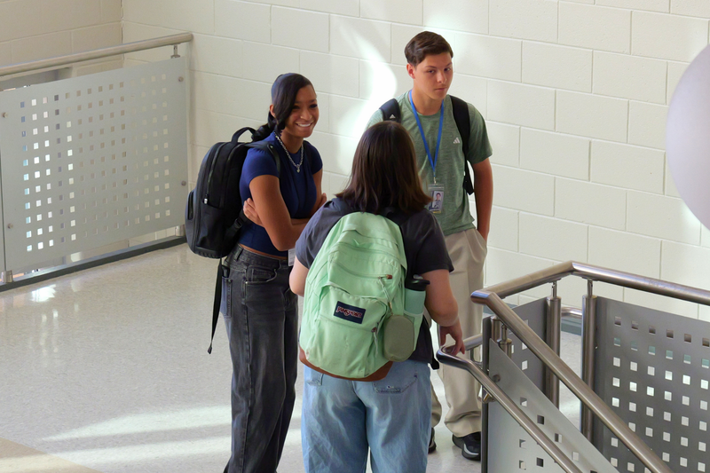 Three students standing and talking in stairway of school.