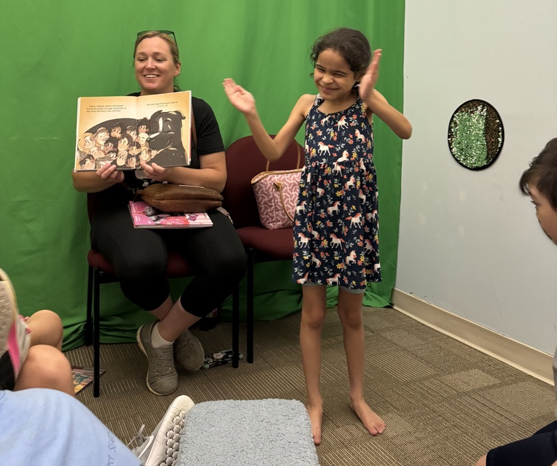 Casey Mason shares her book with students. One girl students is standing with arms raised as if getting ready to clap.