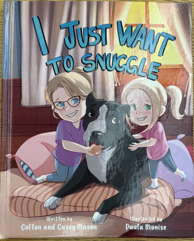 An image of the cover of the book, I Just Want to Snuggle. The cover features two femaile children hugging a black and white dog.