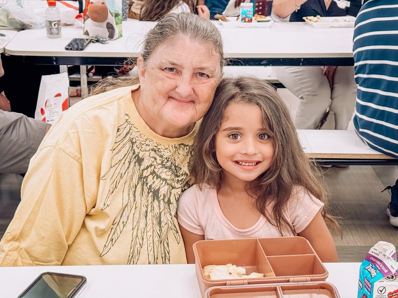 Grandparents Day celebration at elementary school, grandmother with grandchild holding sign. 