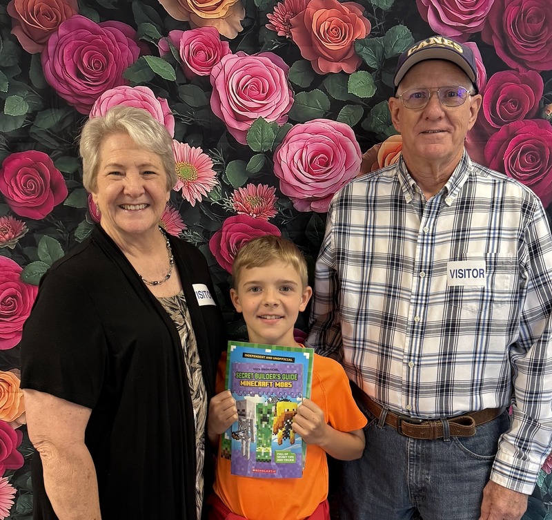 Grandparents Day celebration at elementary school, grandmother with grandchild holding sign. 