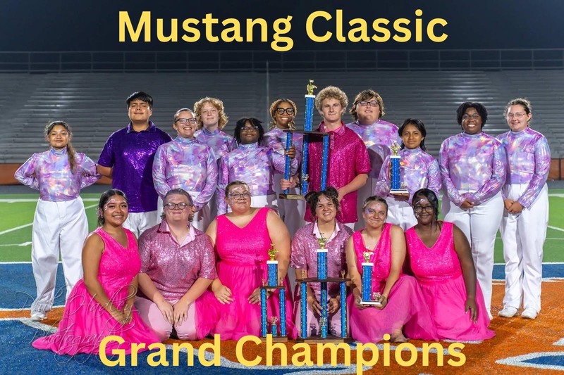 Band students in pink and purple costumes posing with trophy.