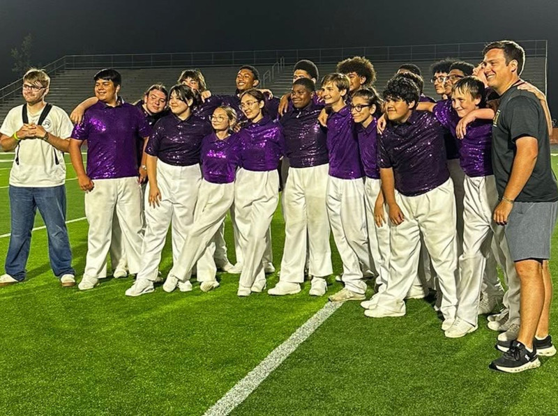 Band students in white and purple posing on football field.