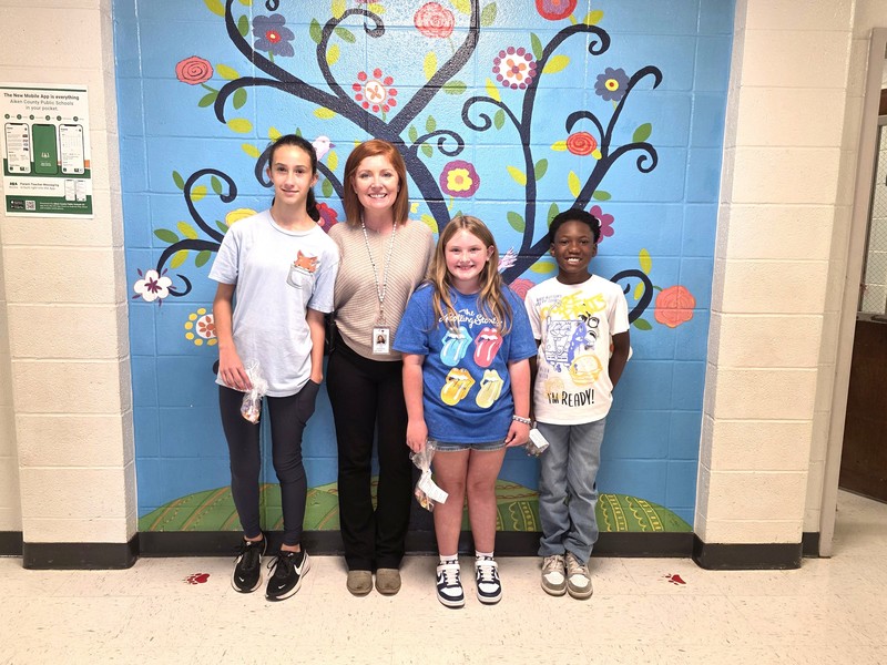 Three  students and principal standing in front of blue wall.