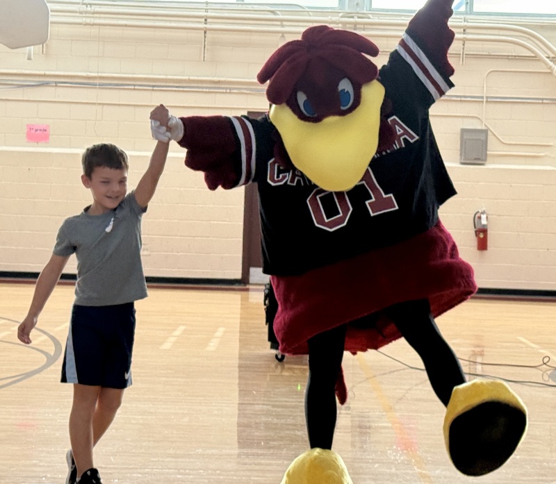 A male student has his arm raised by the USC mascot, Cocky.