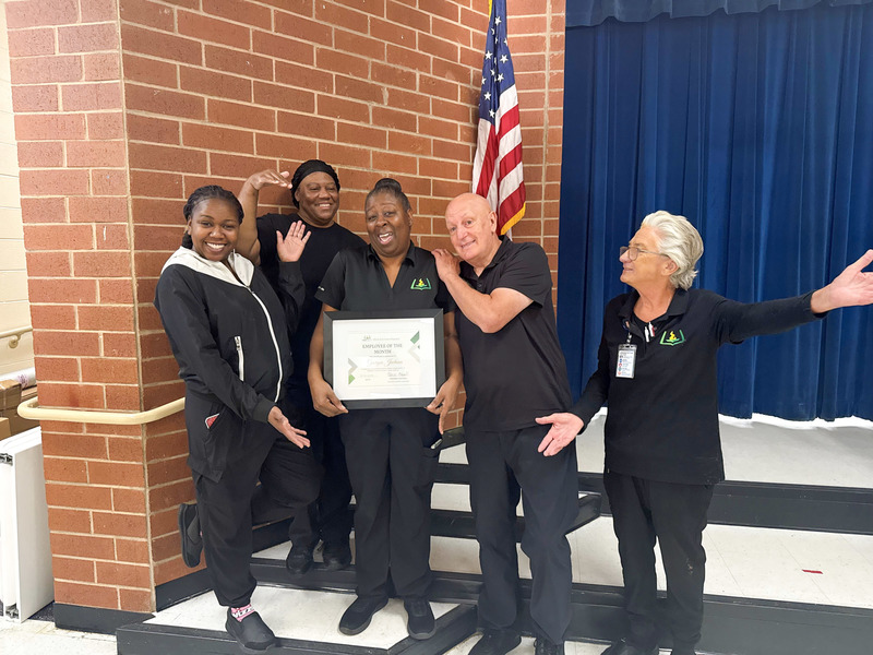 Child Nutrition Professional Georgia Jackson holds a plaque and stands with Mossy Creek Elementary Child Nutrition team members